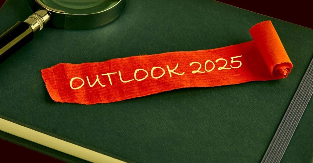 A magnifying glass and piece of paper with text "Outlook 2025" on a desk.